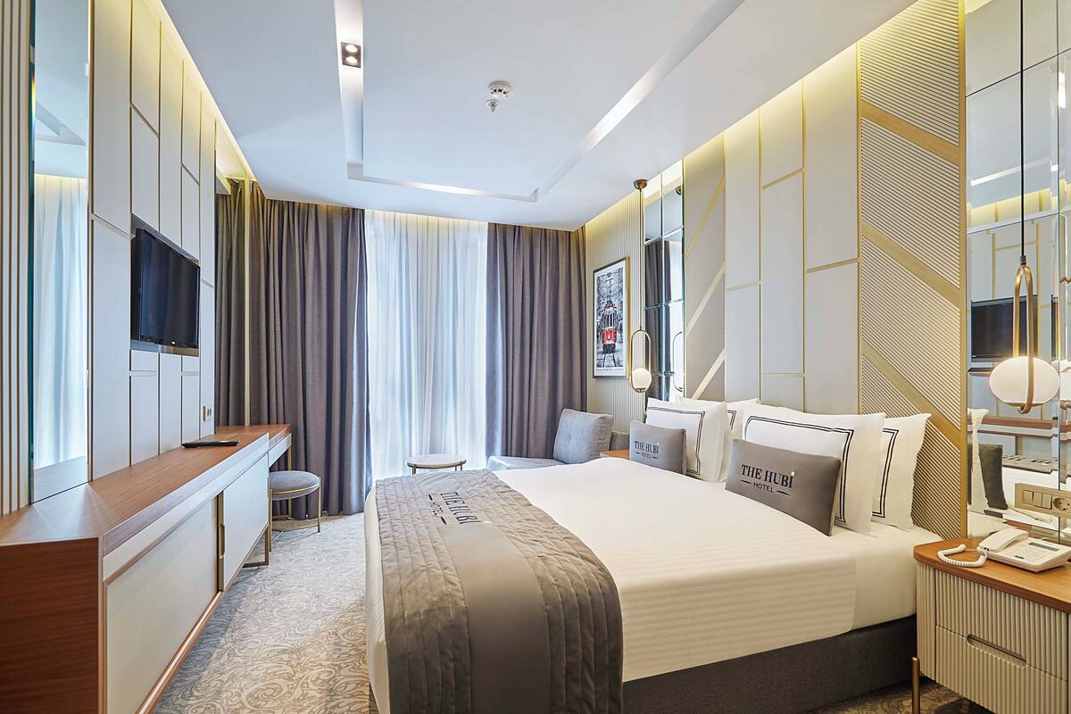 A modern hotel room with a large bed, a desk, a chair, and a TV.