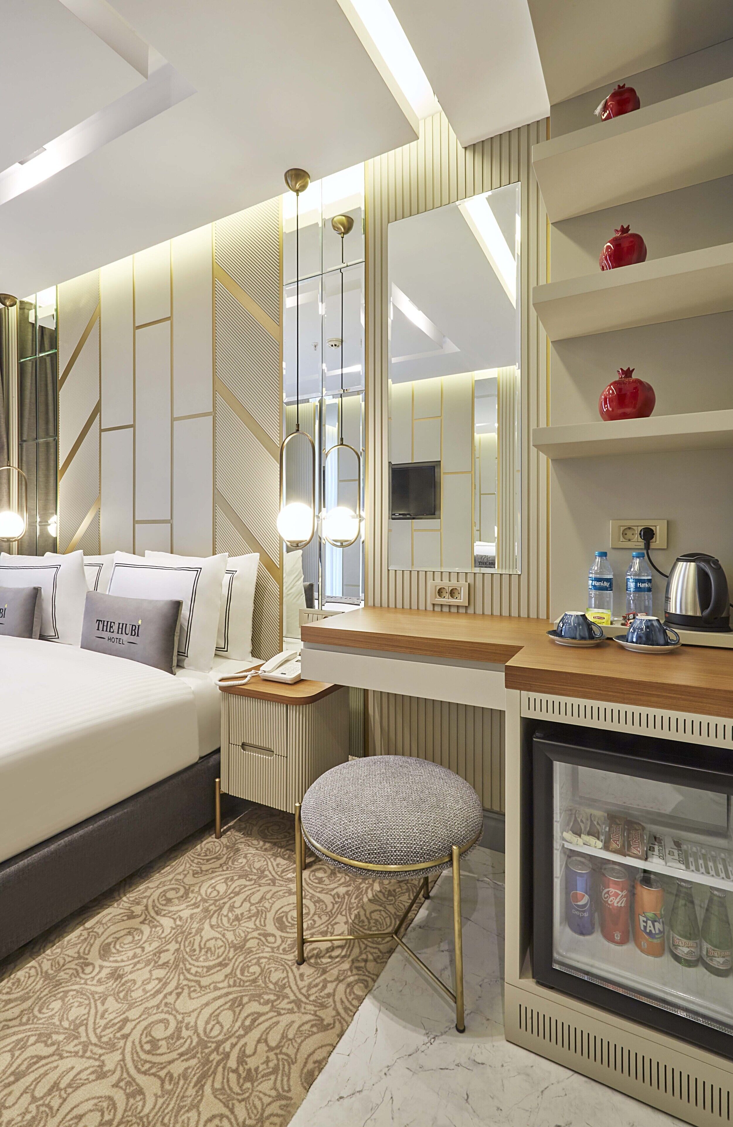 Quarto de hotel moderno com uma cama grande, uma toucador com espelho, um pequeno banquinho, um minibar e uma televisão.