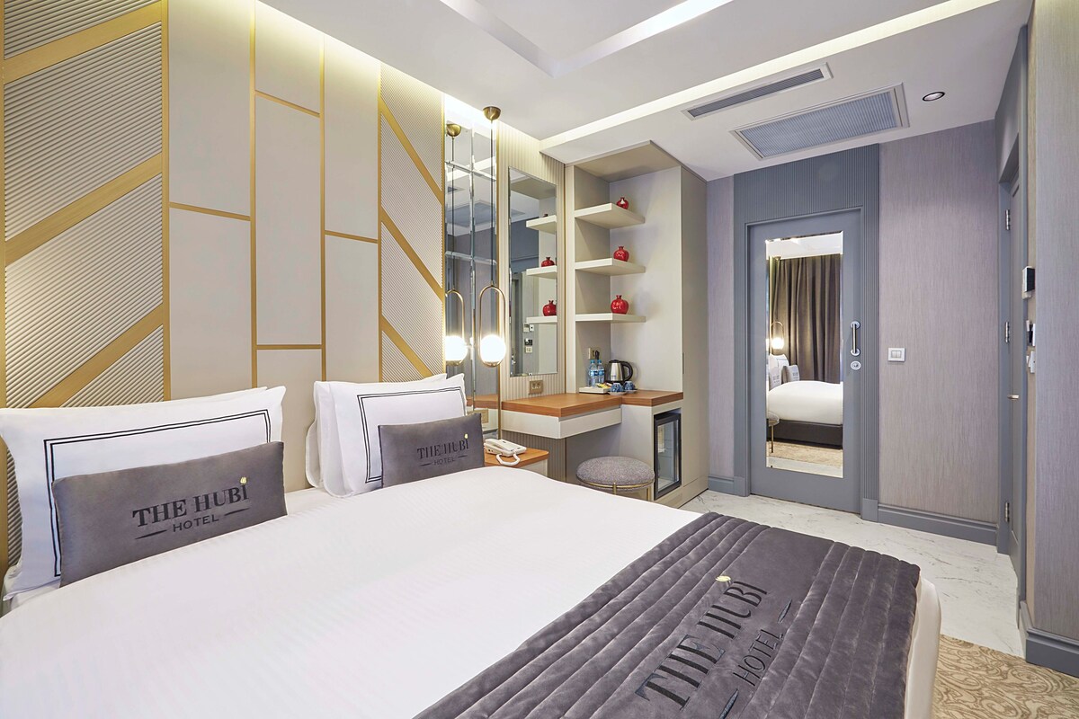 A hotel room with a large bed, a desk with a computer, a mirror, and a wardrobe.