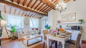 A cozy living room with a wooden ceiling, a dining table set for four, and a kitchen area with a microwave.