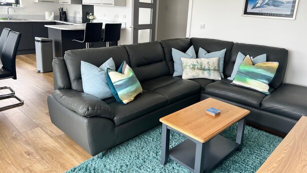A modern living room with a black leather sofa, a wooden coffee table, and a teal rug. - Caledonia Place - Retreat Group (Aviemore)