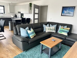 A modern living room with a black leather sofa, a wooden coffee table, and a teal rug.