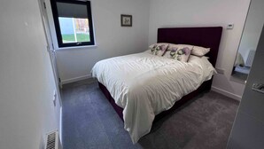 A bedroom with a bed, a window, a radiator, and a mirror. - Caledonia Place - Retreat Group (Aviemore)