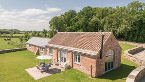 A brick house with a tiled roof, a patio with outdoor furniture, and a stone wall surrounding the property. - Lalo, Pickhill, North York Moors (Thirsk)