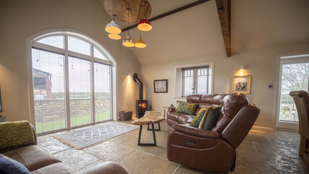 A spacious living room with a leather sofa, a fireplace, and large windows. - Lalo, Pickhill, North York Moors (Thirsk)
