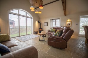 A spacious living room with a leather sofa, a fireplace, and large windows. - Lalo, Pickhill, North York Moors (Thirsk)