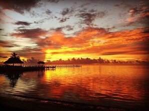 Un atardecer sobre una superficie acuática tranquila con un muelle y estructuras silueteadas contra el cielo.