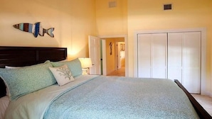 A bedroom with a bed, a nightstand, a lamp, a wardrobe, and a wall decoration. - Jamaican Palm House 3 Bedrooms, 2 Bath, Poolside (Islamorada)