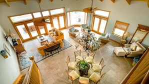 A spacious living area with a high ceiling, large windows, and a dining set in the center.