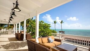 A covered outdoor area with wicker furniture, a view of the ocean, and a white railing.