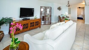 Un salon avec un canapé blanc, un meuble de rangement en bois, un téléviseur et une plante décorative.