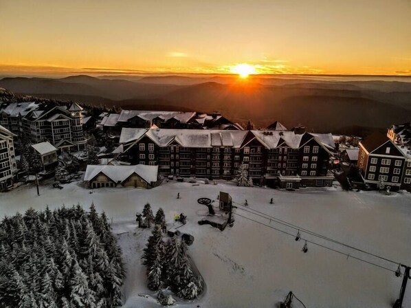 A snow-covered lodge with multiple buildings, a ski lift, and a sunset in the background.