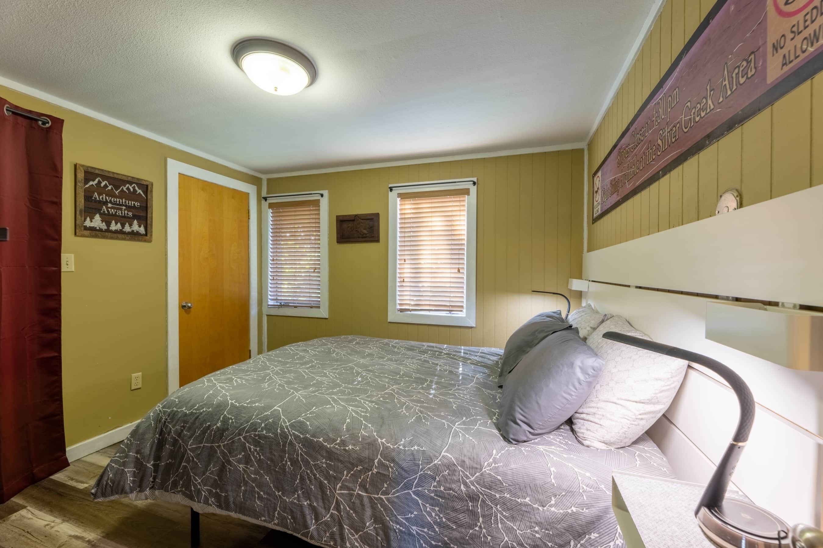 Un dormitorio con cama, mesita de noche, lámpara, puerta y una pared con un cartel.