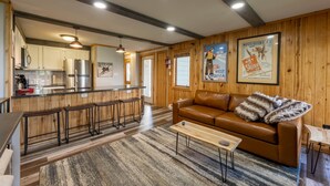 Eine moderne Küche mit Bar, ein braunes Ledersofa und eine Holzwand mit Postern.