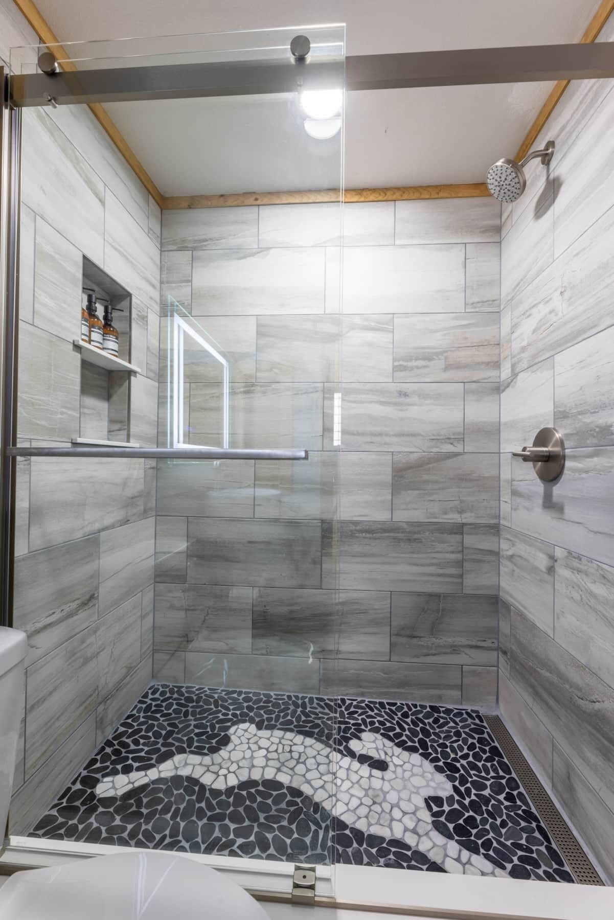 A modern shower room with a glass door, marble tiles, and a mosaic floor design.