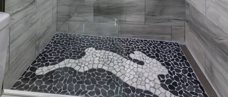 A modern shower room with a glass door, marble tiles, and a mosaic floor design.