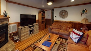 Ein gemütliches Wohnzimmer mit Kamin, einer Holz-Unterhaltungseinrichtung und einem großen Fernseher.