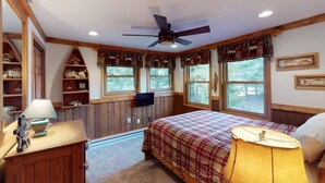 Ein Schlafzimmer mit Bett, Schreibtisch, Lampe, Deckenventilator und Fernseher.