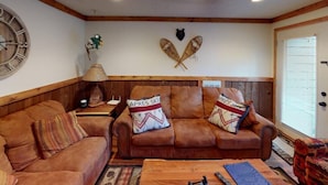 Ein gemütliches Wohnzimmer mit zwei braunen Ledersofas, einem Holztisch und einer Wanduhr.