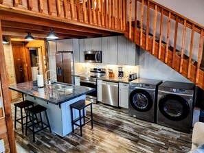 A modern kitchen with a central island, stainless steel appliances, and a wooden staircase. - PowderMonkey 2br/2ba+Loft - Ski out & PET friendly (Snowshoe)