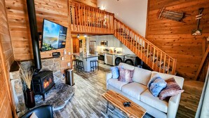 A cozy cabin interior with a living area, kitchen, and a staircase.