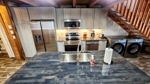 A modern kitchen with stainless steel appliances, a central island, and a wooden staircase.