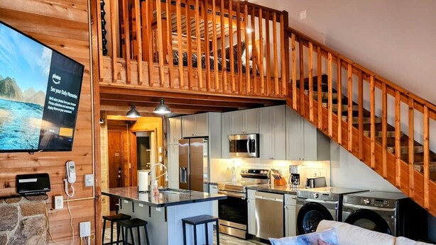 A spacious living area with a kitchen, a dining area, and a staircase leading to an upper level.