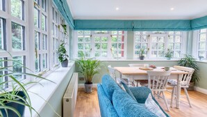 Une pièce lumineuse avec une grande fenêtre, une table en bois, un canapé bleu et plusieurs plantes en pot.
