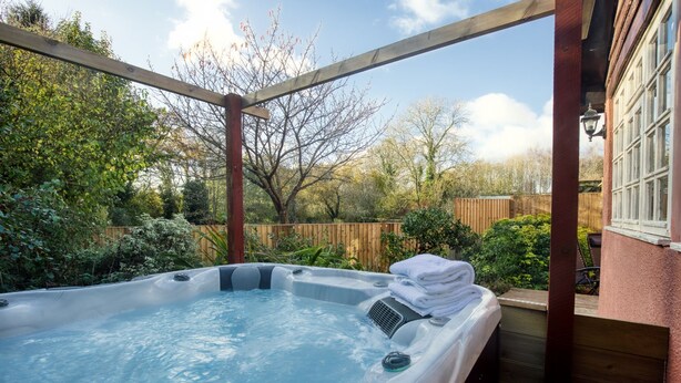 Un bain à remous situé dans un espace extérieur abrité, doté d’une terrasse en bois, et entouré d’arbres et d’une clôture en bois.