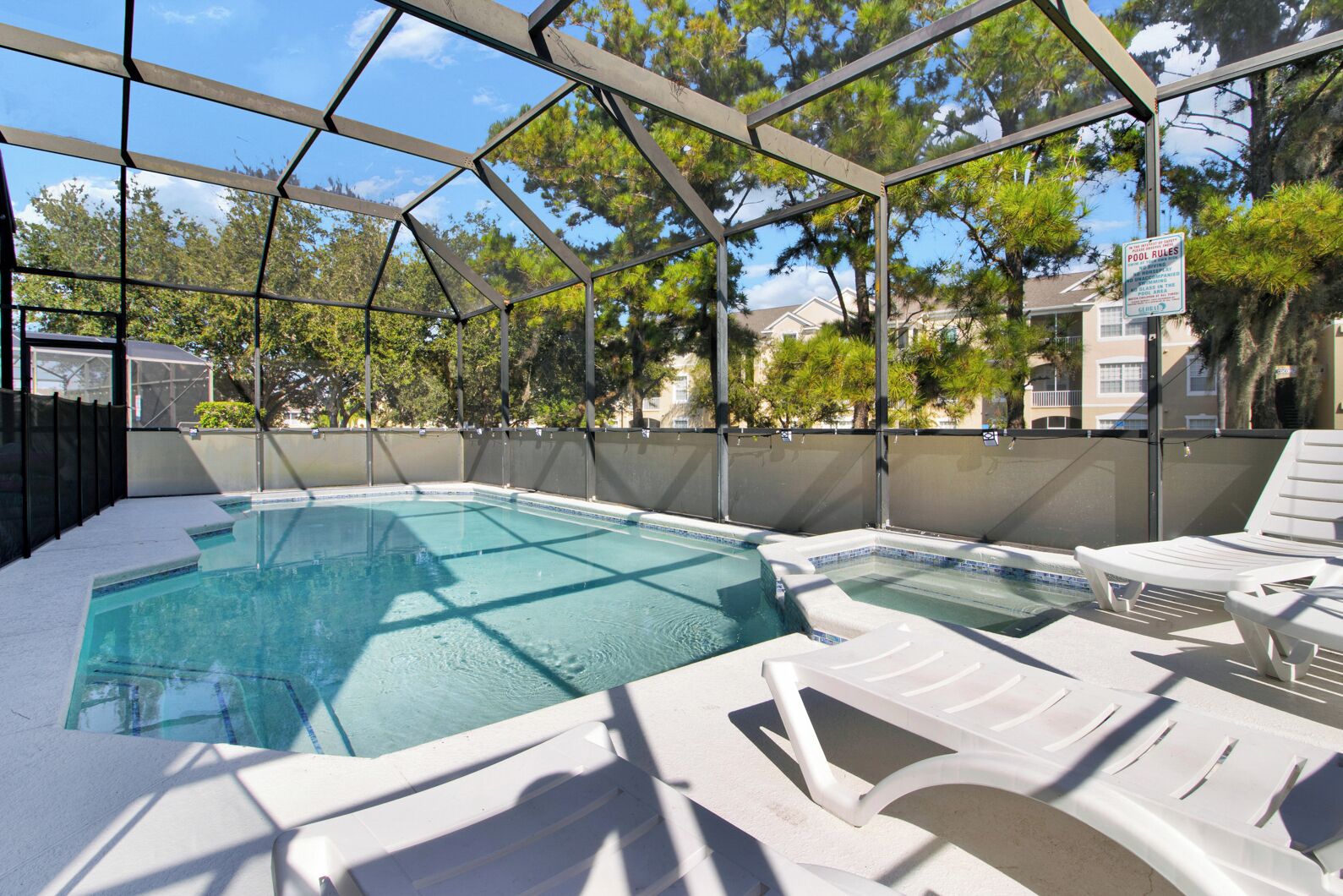 An outdoor swimming pool with a covered area, lounge chairs, and a pool rule sign.