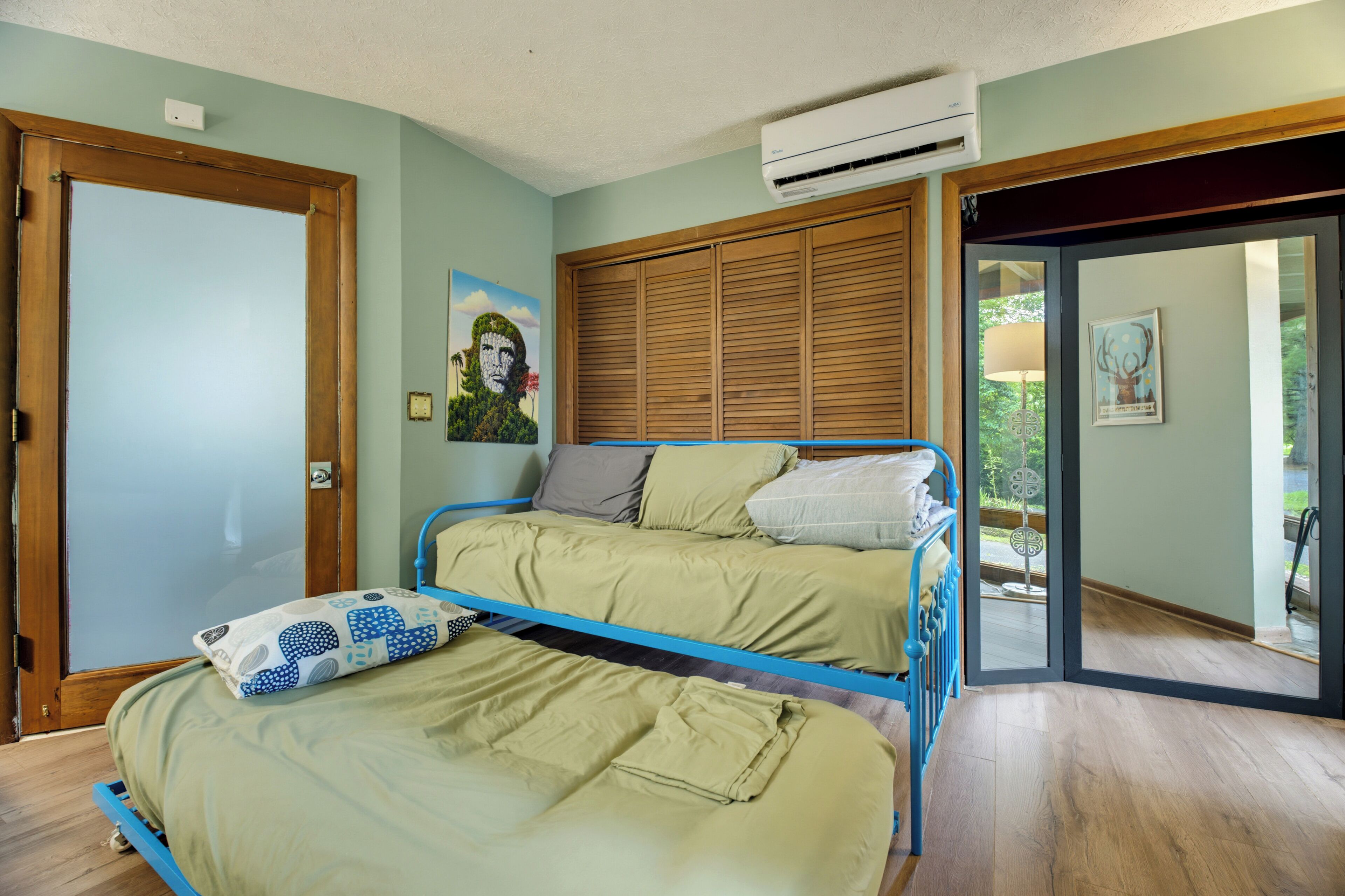 Une chambre avec deux lits, une armoire en bois, un appareil de climatisation et une porte donnant sur un balcon.