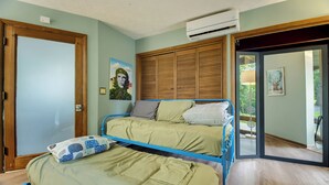 A bedroom with two beds, a wooden wardrobe, an air conditioning unit, and a door leading to a balcony.