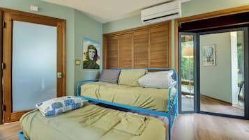 Une chambre avec deux lits, une armoire en bois, un appareil de climatisation et une porte donnant sur un balcon.