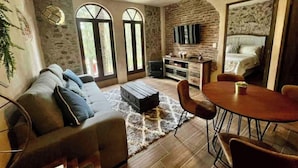 A cozy living room with a sofa, a coffee table, and a dining area with chairs. There is a stone wall and a bed in the background. - Incredible Loft in ValQuirico!  (Xoxtla)