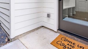 Une façade blanche avec une porte-fenêtre coulissante et un paillasson portant un message.