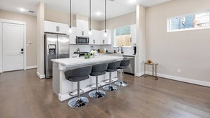 Une cuisine moderne avec des meubles blancs, des appareils en acier inoxydable et un coin bar équipé de tabourets.