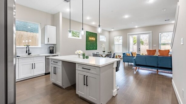 Une cuisine moderne avec des meubles blancs, un îlot central, des luminaires suspendus et un coin repas agrémenté d’un canapé bleu.