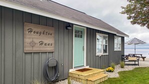 Una casa con un letrero de madera que dice "Houghton House", una puerta principal, un banco, un paraguas y un pequeño jardín.