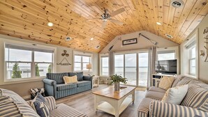 Una sala de estar acogedora con sofás a rayas, techo de madera y ventanas amplias con vista a un cuerpo de agua.