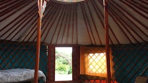 A traditional yurt interior with a bed, a small table, and a window with a lattice design.
