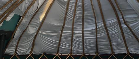 Interno di una yurt tradizionale con un letto, una testata in legno e un lucernario circolare.
