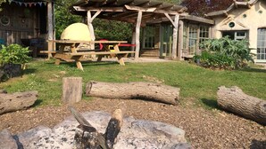 A rustic outdoor setting with a wooden pergola, picnic table, and barbecue grill.