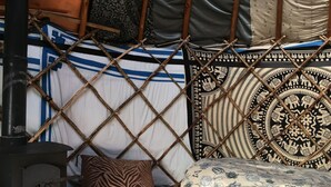 A traditional tent with a central stove, patterned cushions, and a bed with a floral bedspread.