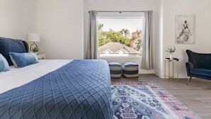 A bedroom with a large bed, a view of the outside, a chair, and a small table. - Alim Pad 3: Brand New Modern house near downtown (Houston)