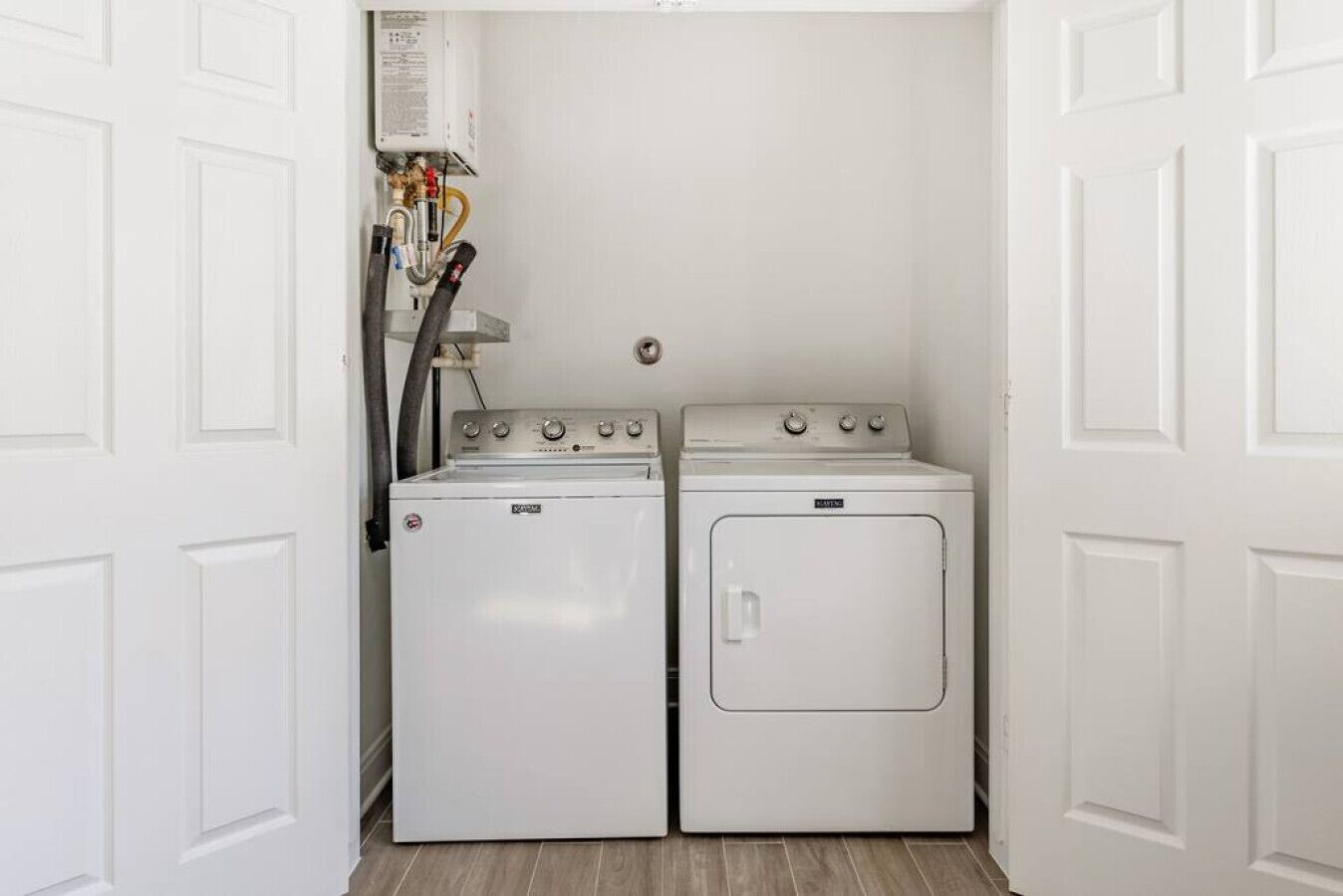 A laundry room with two white washing machines and a dryer, a water heater, and a wall-mounted vent.
