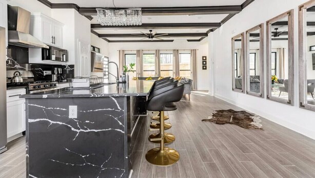 A modern kitchen with a marble island, black bar stools, and a chandelier. - Alim Pad 3: Brand New Modern house near downtown (Houston)