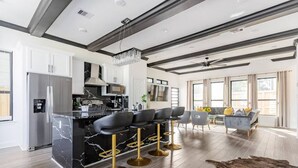 A modern kitchen with a marble island, bar stools, and a dining area with a sofa and chairs. - Alim Pad 3: Brand New Modern house near downtown (Houston)