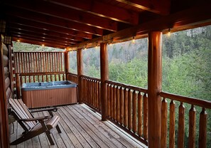 Relax in a hot tub surrounded by lush greenery on a deck with a wooden railing.
