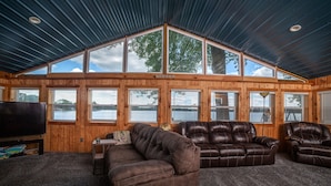 L’intérieur d’une cabane en rondins, avec une grande fenêtre, des canapés en cuir et un téléviseur.