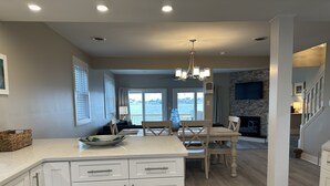 Una cocina amplia con muebles blancos, un comedor con sillas de madera y vistas al agua a través de grandes ventanales.
